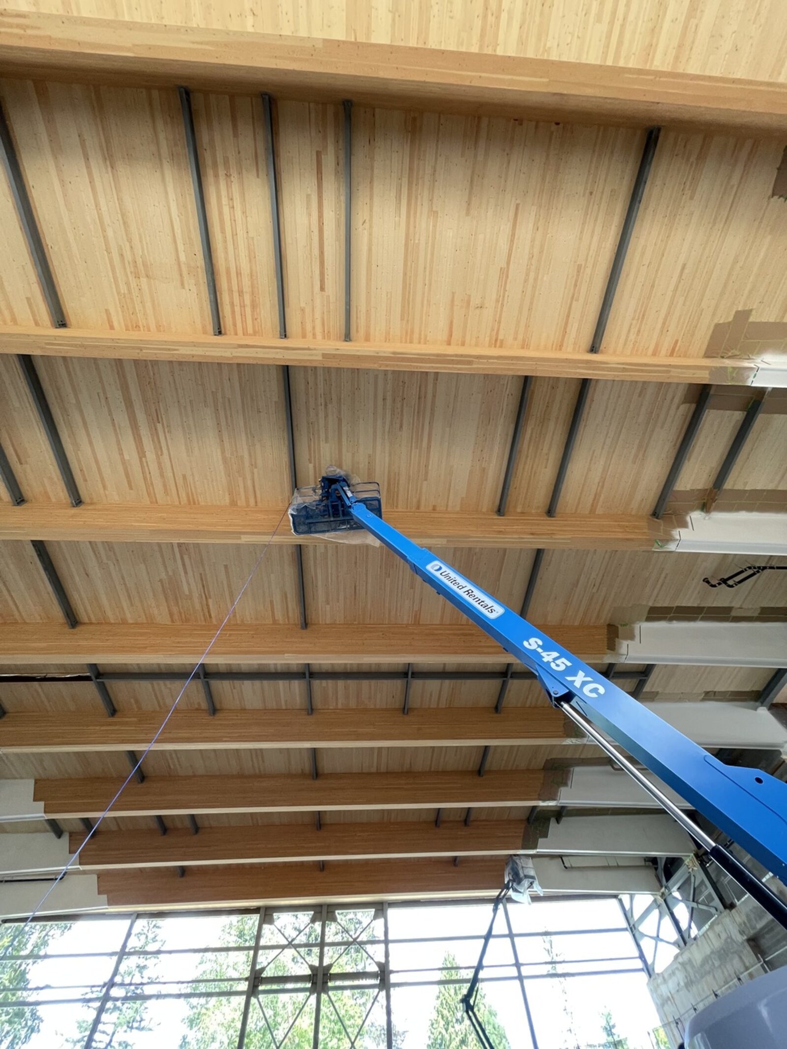 Arched mass-timber ceiling in a large open building, with a boom lift raised to the underside of the glulam beams.