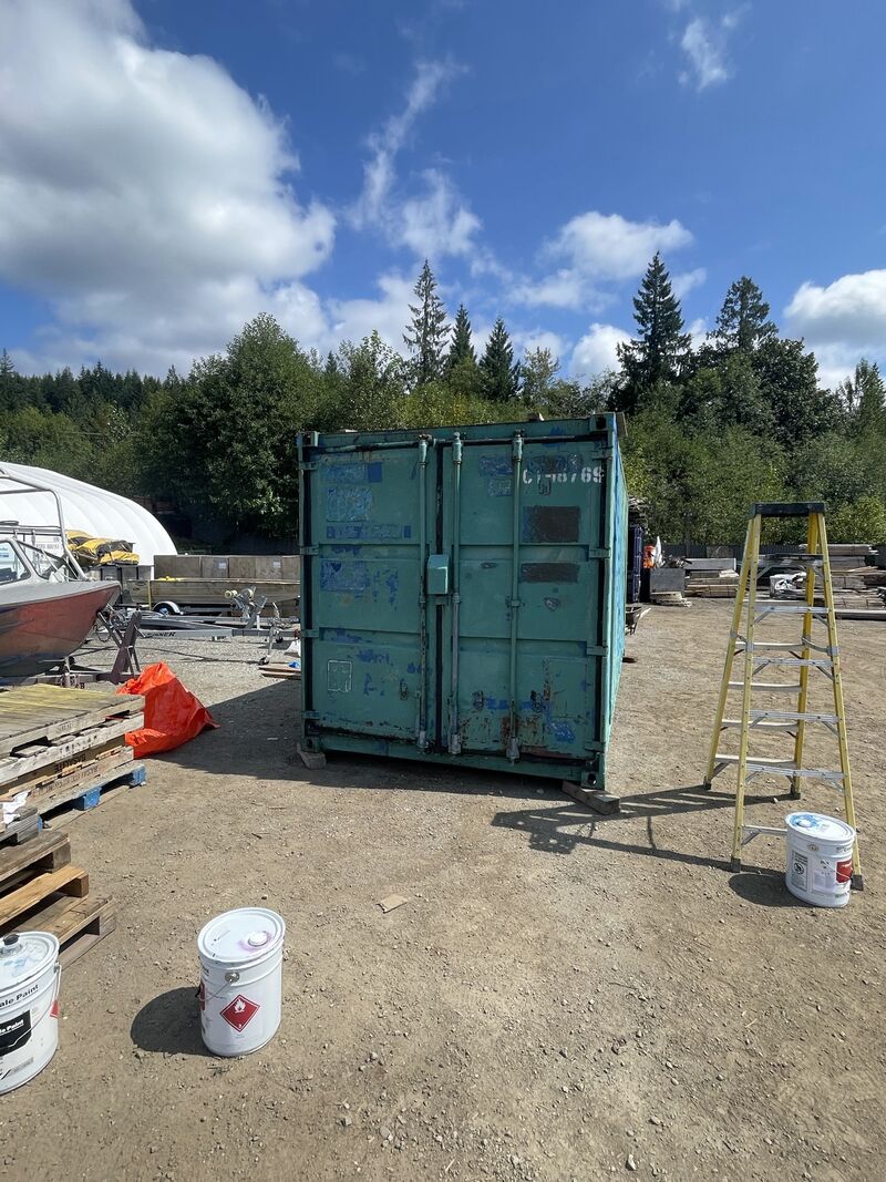 Door end of the green container before painting, with a stepladder and paint pails beside it.