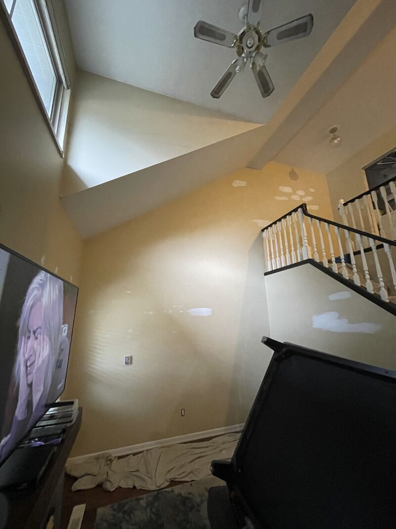 Before: a tall yellow stairwell wall with a ceiling fan above and patch marks on the paint.