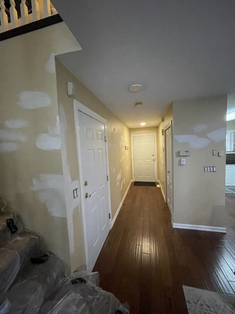 A downstairs hallway with yellow walls and white patch marks before painting.