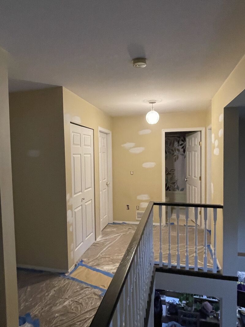 Before: an upstairs hallway with yellow walls, patch marks, and plastic sheeting and tape on the floor.