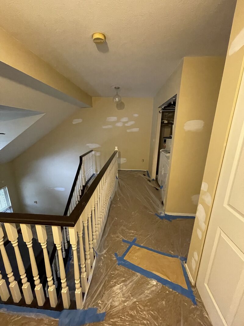 Before: a stair landing with yellow walls, patches, and the floor masked with plastic and tape.