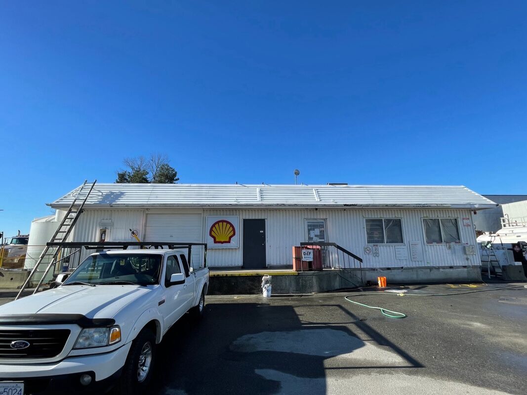 A long single-storey commercial building with white siding and a cleaned metal roof, a work truck parked in front.
