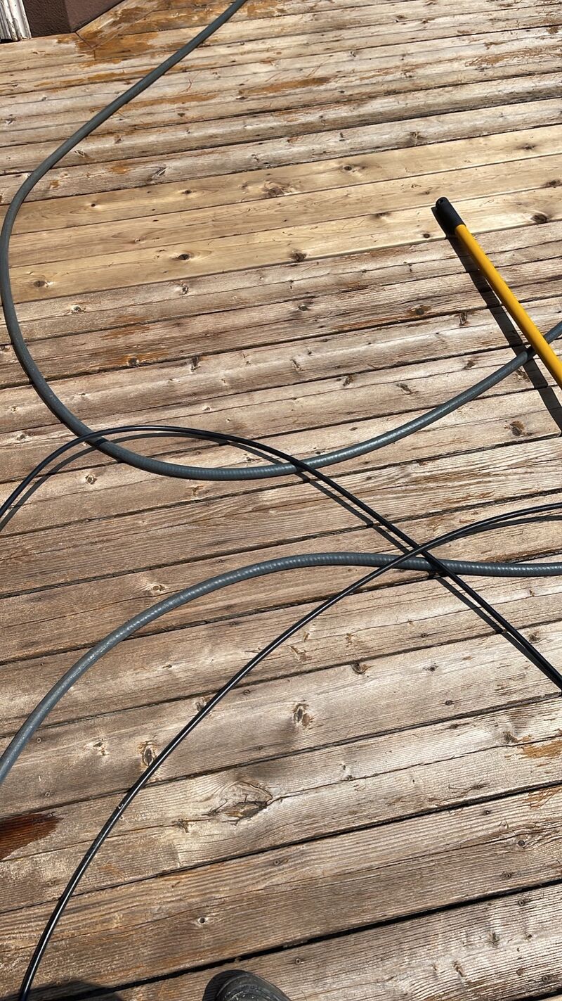Weathered grey deck boards with a pressure washer hose and wand laid across them.