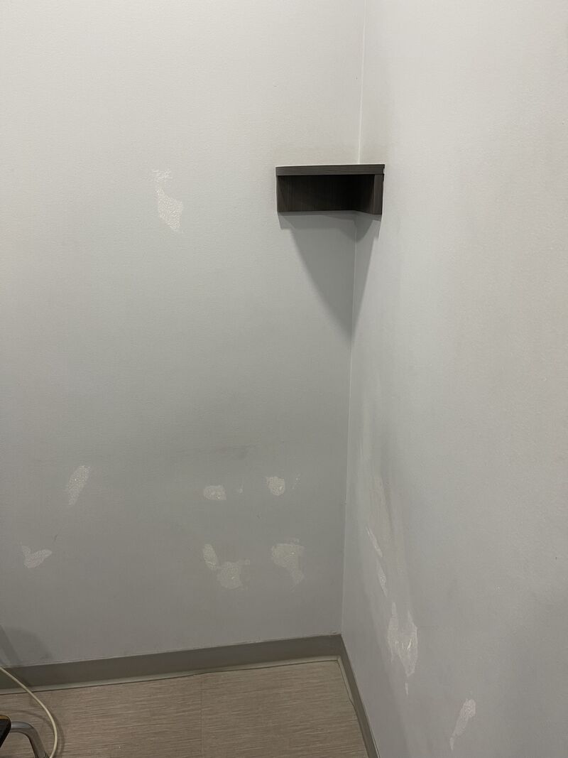 Corner of a treatment room with patches on the wall and a small shelf.