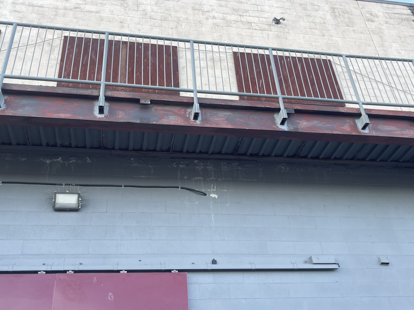A long structural steel beam and railing running the length of a building, prepped and primed.